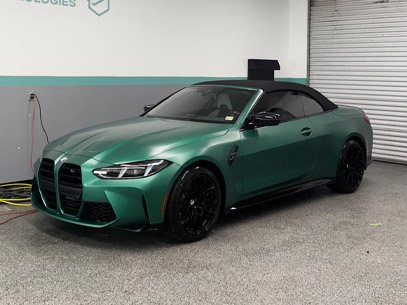 A green BMW convertible with a black soft top is parked indoors next to a closed garage door.