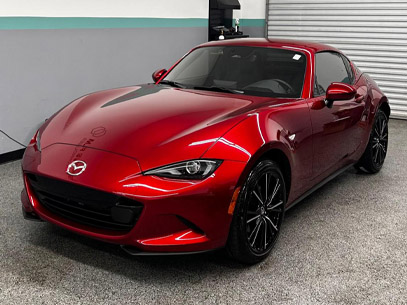 A red Mazda MX-5 Miata sports car is parked indoors on a gray speckled floor near a closed garage door.