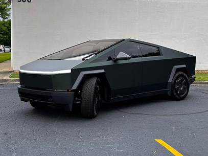 A matte black Tesla Cybertruck is parked in a lot near a light gray concrete wall.